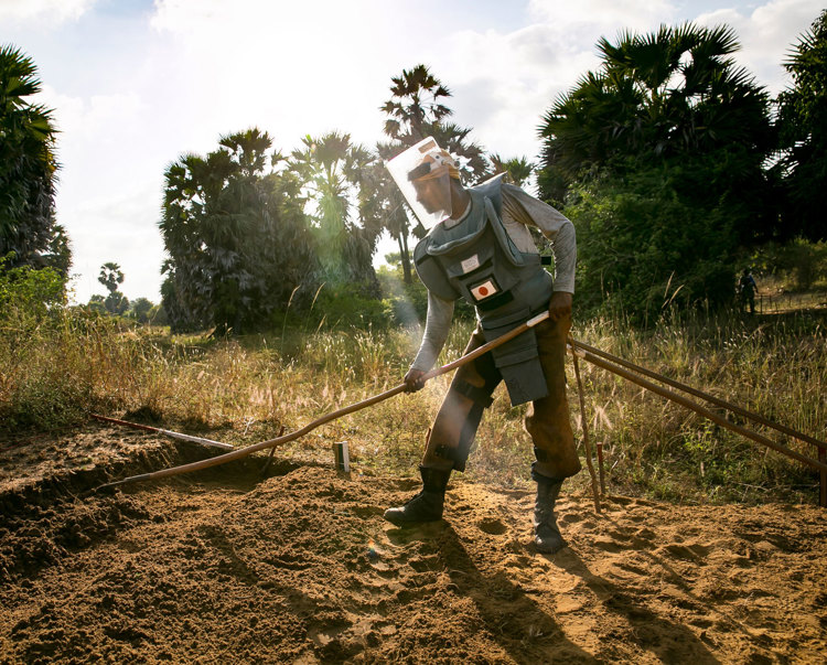 A deminer wearing PPE rakes the soil